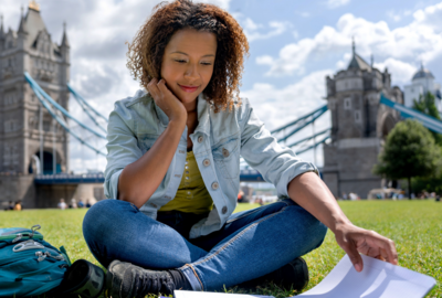 Englisch lernen macht Spaß, besonders in einem englischsprachigen Land. Hier lernt eine Frau auf der Wiese in London Englisch. Im Hintergrund ist die berühmte Tower Bridge.